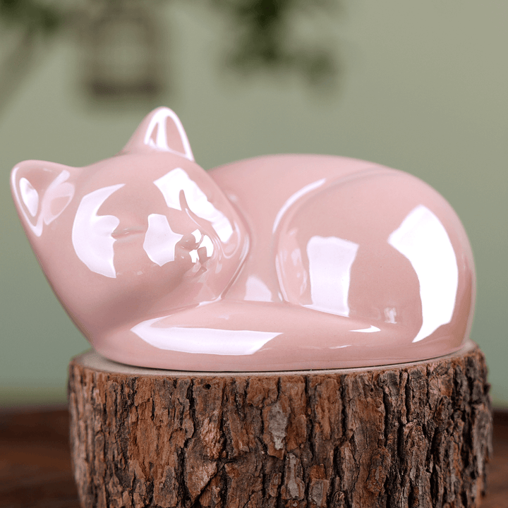 Pink ceramic cat figurine on a wooden stump with a blurred green background